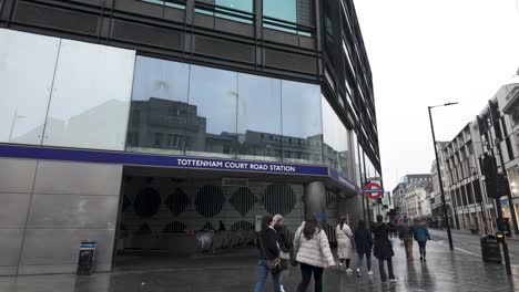 Tottenham-Court-Road-station-entrance-on-a-cloudy-day-in-London,-pedestrians-walking-past