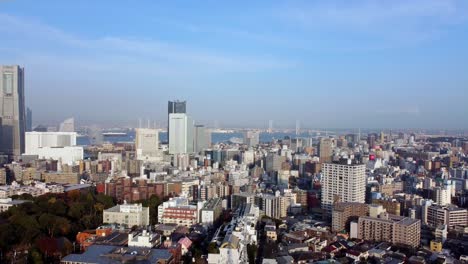 A-bustling-cityscape-with-skyscrapers-under-a-clear-sky-at-midday,-urban-expanse-spreading-to-the-horizon,-aerial-view