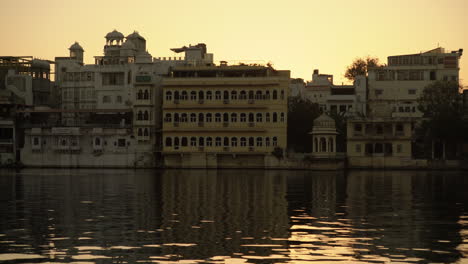 As-the-sun-dips-below-Lake-Pichola-in-Udaipur,-India,-graceful-ducks-glide-across-the-water,-complementing-the-serene-backdrop-of-stunning-architecture,-resulting-in-a-captivating-sight