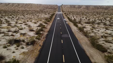 Drone-aerial-shot-navigating-through-the-expansive-landscape-of-Anza-Borrego-desert-road-near-Blair-Valley,-California,-with-a-white-car-driving-along-the-road
