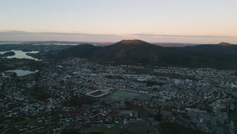 Bergen,-Noruega-Al-Atardecer-Con-Las-Luces-De-La-Ciudad-Y-Las-Colinas-Circundantes,-Vista-Aérea