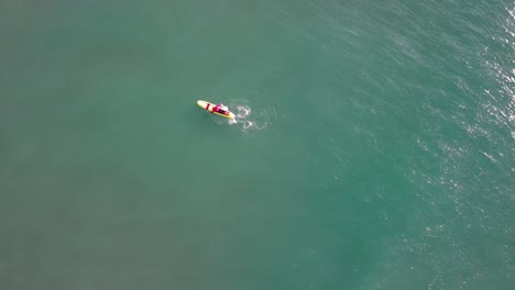 A-lone-surfer-on-a-colorful-board-in-the-clear-waters-of-port-ginesta,-barcelona,-aerial-view