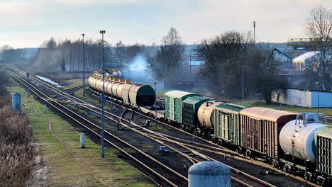 Freight-train-loaded-with-industrial-goods-departing-smoothly,-wagons-pulled-by-diesel-locomotive