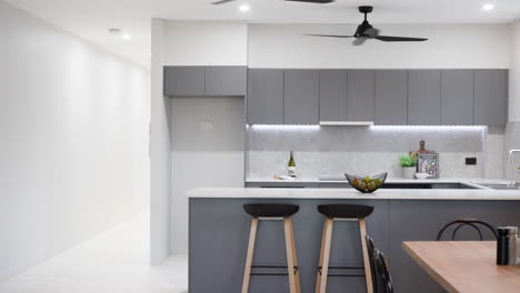 Moderne-Luxuriöse-Graue-Apartmentküche-Mit-Pfannentisch-Und-Schwarzen-Stühlen-Mit-Passenden-Hockern-Und-Unterschrankbeleuchtung
