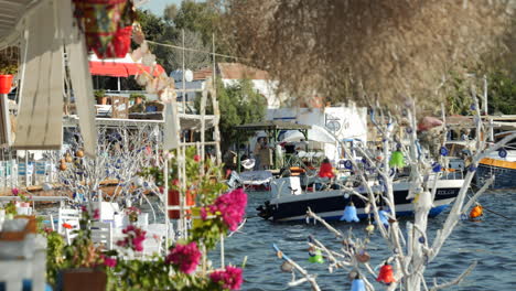 Boat-Floating-In-The-Sea-Behind-The-Plants-At-Seafront-Restaurant-In-Gumusluk,-Turkey