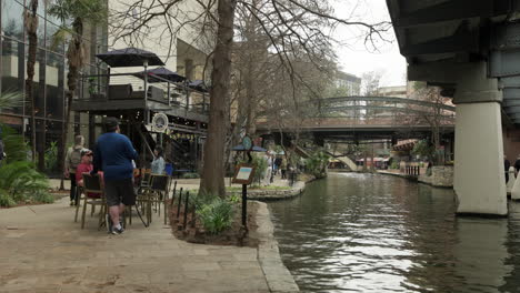 People-Walk-and-Boat-Along-River-Walk-in-San-Antonio,-Texas,-USA