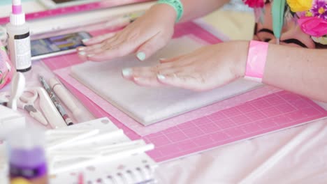 Hands-creating-a-scrapbook-on-pink-mat-with-crafting-tools-around,-bright-colors
