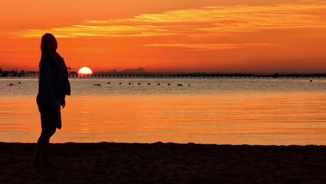 The-silhouette-of-a-lady-on-an-ocean-beach-against-an-orange-sky