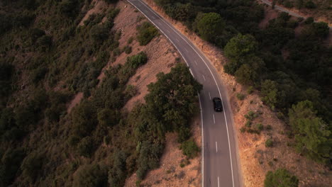 Aerial-View-of-Black-Car-Driving-Along-Mountain-Pass-At-Sunset,-Road-Trip-Along-Mountainside-Roadway