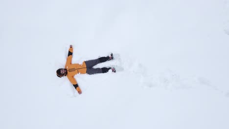 Man-in-a-yellow-snow-jacket-falls-back-into-the-snow-to-make-an-angel