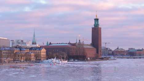 Red-brick-Stockholm-City-Hall-with-lantern-topped-tower,-aerial-over-iced-lake