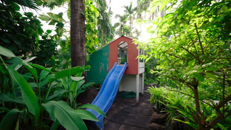 Golden-Hour-Large-Painted-Wooden-Cubby-House-Playground-With-Slide-And-Sun-Flare-in-Tropical-Backyard