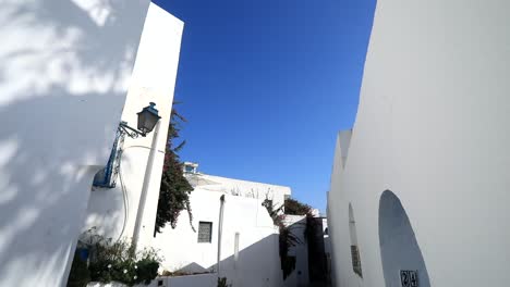 Bright-sunny-day-on-a-narrow-street-in-Sidi-Bou-Said,-Tunisia,-with-white-walls-and-blue-accents