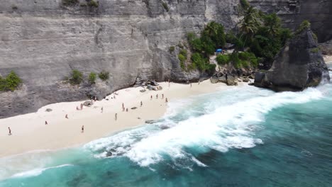 Menschen-Am-Weißen-Sandstrand-Diamond-Beach-Mit-Kalksteinfelsen-Im-Hintergrund,-Nusa-Penida,-Luftaufnahme