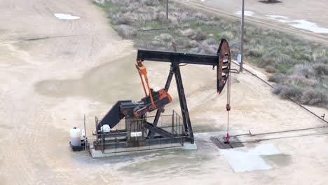 An-oil-pumpjack-in-motion-in-a-desolate-field,-overcast-day,-industrial-scenery,-aerial-view
