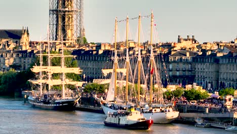 Colonial-sailing-ships-in-the-Garonne-river-during-yearly-Wine-Fair-with-large-crowds,-Aerial-dolly-left-shot