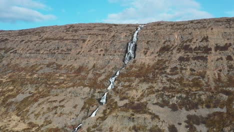 Cascada-En-Un-Sereno-Fiordo-Islandés,-Exuberante-Paisaje-Bajo-Un-Cielo-Despejado,-Vista-Aérea