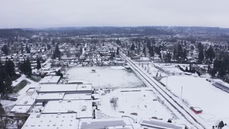 Luftaufnahme-über-Einer-Kleinstadt-Highschool-An-Einem-Verschneiten-Tag-Mit-Einem-Fluss-Im-Hintergrund