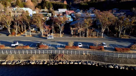 Coastal-road-with-vehicles-and-adjacent-seaside,-residential-area-backdrop,-golden-hour-light,-aerial-view