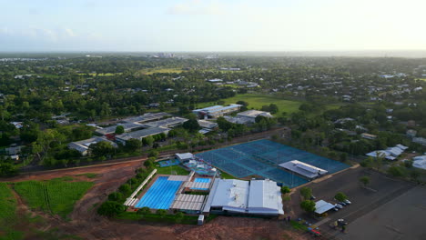 Drone-Aéreo-De-Piscina-Recreativa-Y-Canchas-De-Tenis-Con-Brillo-De-Hora-Dorada-En-El-Cielo-Del-Horizonte,-Aléjese-Del-Territorio-Norteño-De-Australia