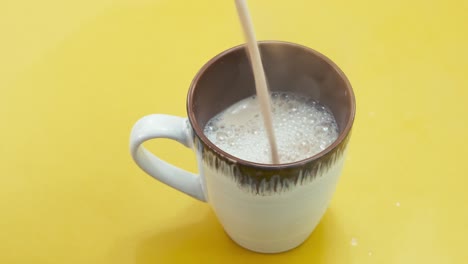 Pouring-Hot-Creamy-Coffee-Into-Cup-On-Yellow-Surface