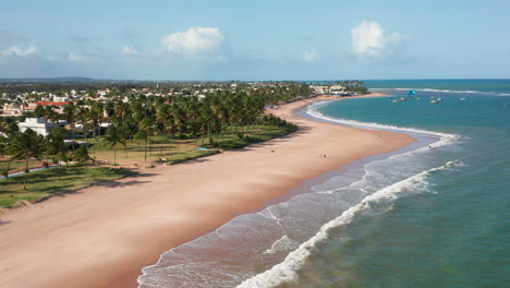 Aerial-view-of-the-beach,-waves-and-a-large-green-area-with-palm-trees,-a-person-practing-kite-surf-and-the-city-at-background,-Guarajuba,-Bahia,-Brazil