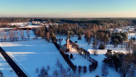 Church-with-a-red-roof-and-black-steeple-in-the-middle-of-a-snowy-field,-with-a-pink-sky-in-the-background