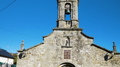 Medium-tilt-down-along-bell-tower-entrance-of-San-Xoan-de-Rio-with-effigy-carved-statue-and-stained-glass-window