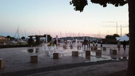 Balatonfured,-Plaza-De-Vela-Durante-El-Atardecer-Temprano-Con-Una-Fuente-Y-El-Puerto-Deportivo-Al-Fondo,-Hungría