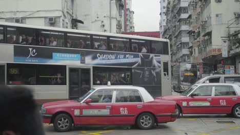 Taxi-cabs-with-traditional-red-color-drive-into-an-intersection-with-traffic-next-to-bus---slow-motion