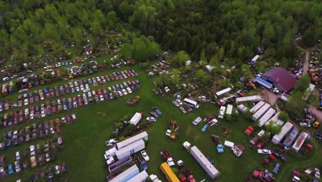 Aerial-shot-of-an-abandoned-scrap-yard-with-trucks,-Trailers,-and-old-cars-rotting-away-and-overgrown-with-trees