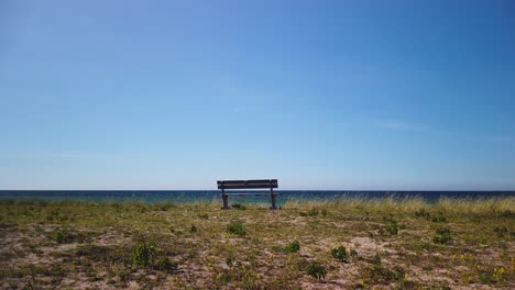 Solitary-bench-overlooking-the-calm-Baltic-Sea-on-Gotland's-Irevik-shore,-clear-blue-sky