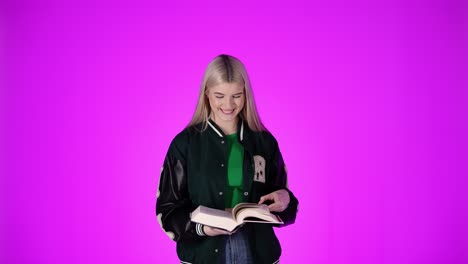 Cute-girl-laughing,-looking-at-camera-and-reading-a-large-book,-studio-shot