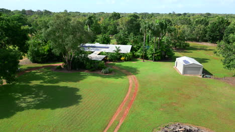 Aerial-drone-of-Rural-Tropical-Estate-Exterior-Dirt-Driveway-Across-Open-Field,-Dolly-Establish
