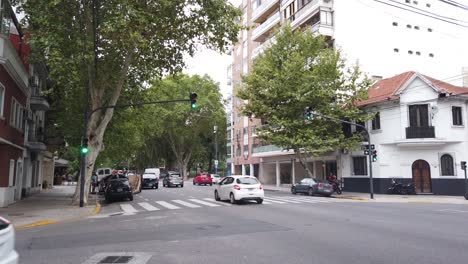 Calles-De-La-Ciudad-De-Buenos-Aires-Barrio-De-Flores-Argentina,-Autos-Circulan-Por-Avenida-área-Urbana-Asfaltada,-Verano-En-La-Capital-Sudamericana,-árboles-Y-Semáforos