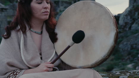 Mujer-Espiritual-Tocando-Pacíficamente-Un-Tambor-Chamánico-En-Un-Hermoso-Pueblo-Medieval-Con-Una-Toma-De-Detalle-Medio-Cercana