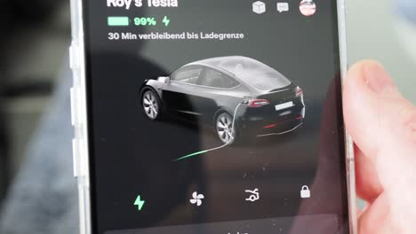 Männliche-Hand-Hält-Smartphone-Mit-Tesla-App-Beim-Ladevorgang