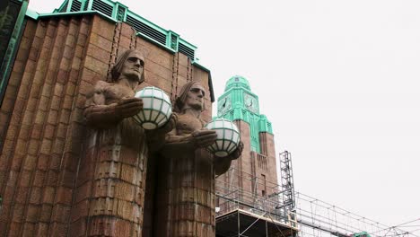 Art-deco-statues-holding-lamps-at-Helsinki-Central-Station,-cloudy-sky-backdrop