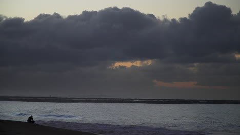 Persona-Solitaria-En-Seal-Beach-Al-Atardecer-Con-Pesadas-Nubes-Sobre-El-Horizonte,-Tranquila-Escena-Oceánica