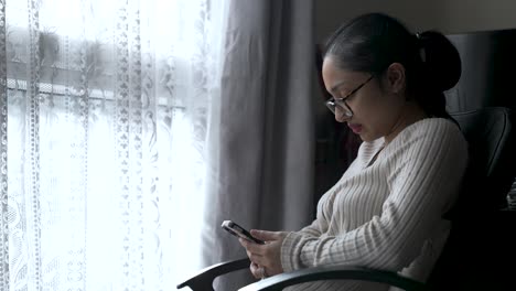 Frau-Im-Pullover-Benutzt-Smartphone-Am-Fenster,-Tageslicht,-Heitere-Stimmung