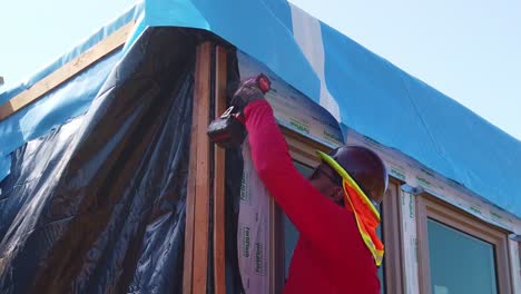 Gimbal-close-up-shot-of-a-construction-worker-using-a-screw-gun-to-secure-the-siding-of-a-housing-module-at-a-pre-fabricated-building-site-in-West-Los-Angeles,-California