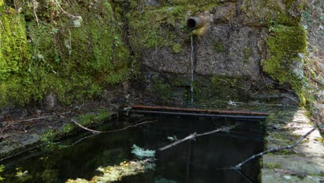 Fuente-Gotea-Agua-Lentamente-Debajo-Del-Puente-Navea-Cubierto-De-Musgo