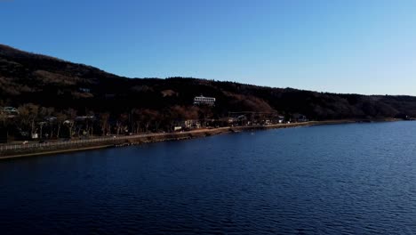 A-serene-lakeside-with-a-road-and-bare-trees-in-late-autumn,-aerial-view