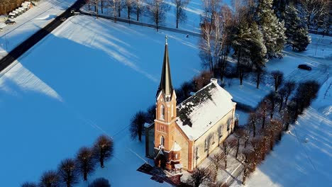 Pequeña-Iglesia-Blanca-Con-Puerta-Roja-Y-Campanario-Negro,-Situada-En-Un-Campo-Nevado