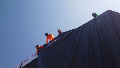 Gimbal-close-up-shot-of-a-construction-crew-securing-a-tarp-over-a-module-at-a-pre-fab-housing-site-in-West-Los-Angeles,-California