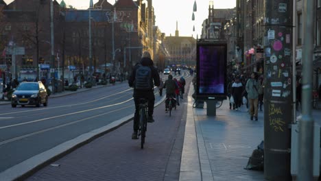 People-on-bicycles-and-walking-down-city-streets-at-sunset-in-Amsterdam,-Netherlands