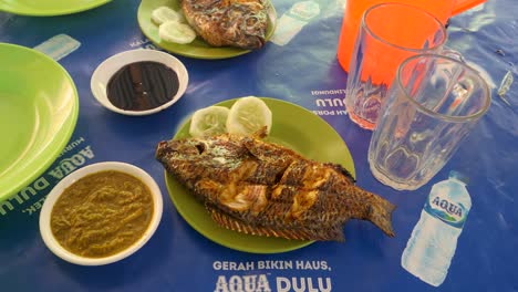 Pescado-A-La-Parrilla-Servido-Con-Sambal-En-Mesa-Azul,-Cocina-Indonesia-En-El-Lago-Toba,-Sumatra