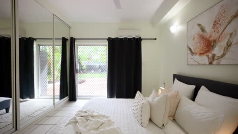 Kleines,-Modernes-Schlafzimmer-In-Einer-Gefliesten-Wohnung-Mit-Spiegelschrank-Und-Elegantem-Gemälde,-Bequemem-Bett-Und-Dunklen-Verdunkelungsvorhängen