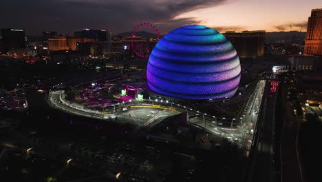 Aerial-view-around-the-illuminated-F1-course-and-the-sphere,-dusk-in-Las-Vegas