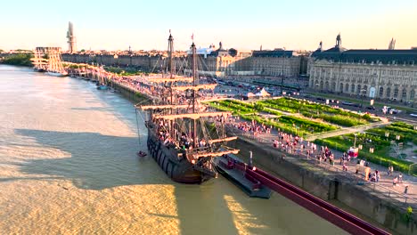 Gran-Velero-Galeón-En-El-Río-Garona-Durante-La-Feria-Anual-Del-Vino-Con-Orilla-Abarrotada,-Toma-Aérea-De-Paso-Elevado